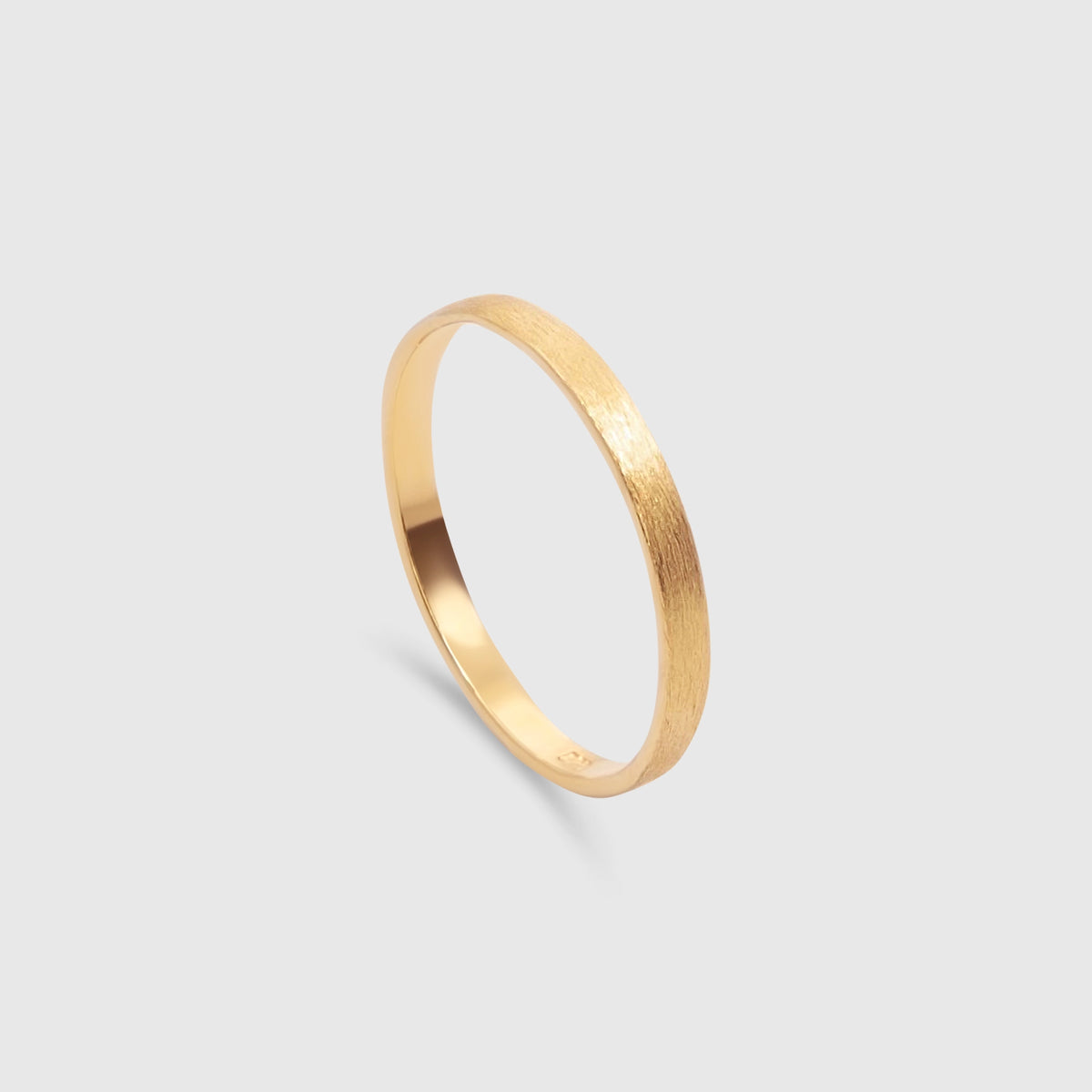 Schlichter goldener Bandring mit mattierter, satinierten Oberfläche vor hellem Hintergrund.