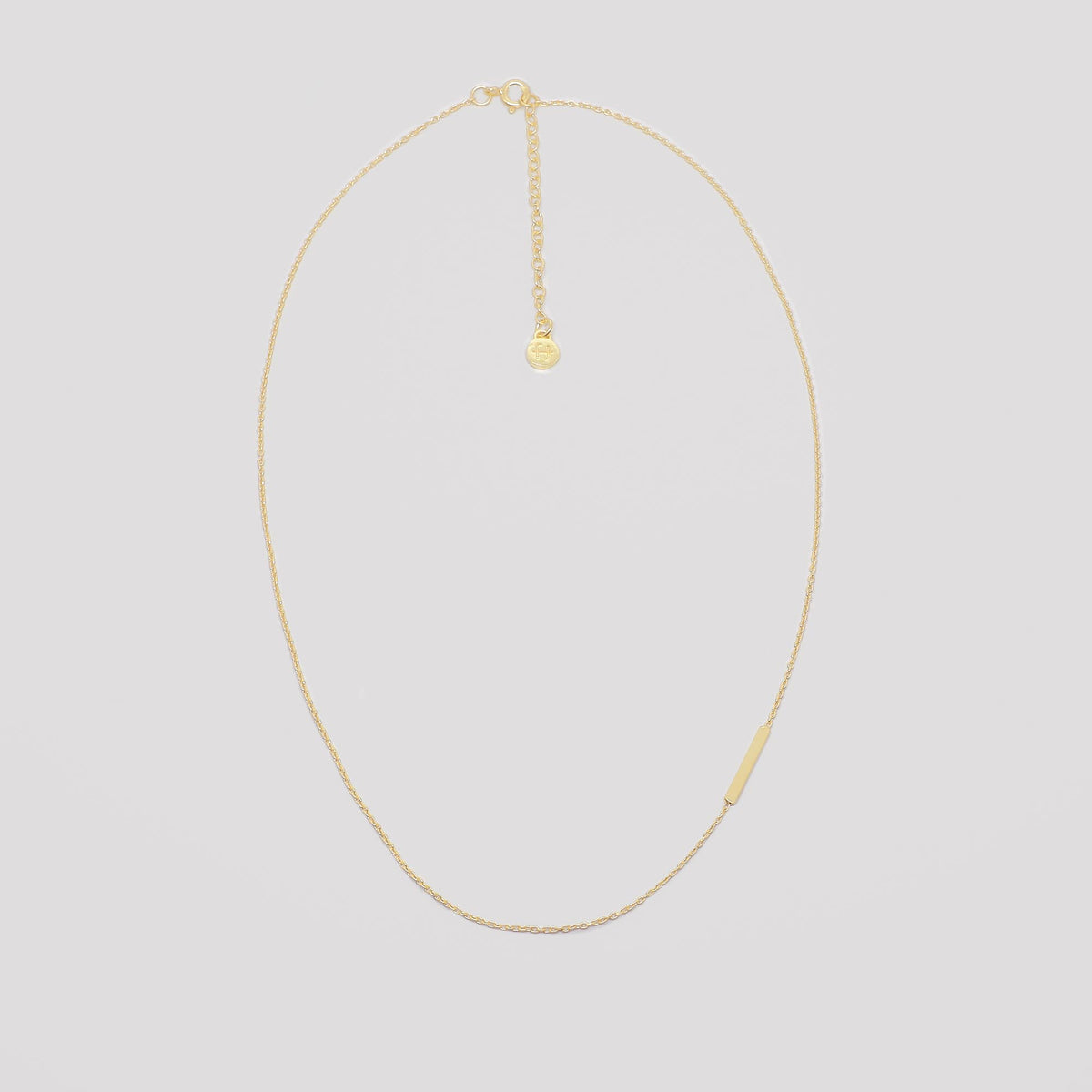 Filigrane Kette in Gold mit querliegendem, satiniertem Stabanhänger vor hellem Hintergrund
