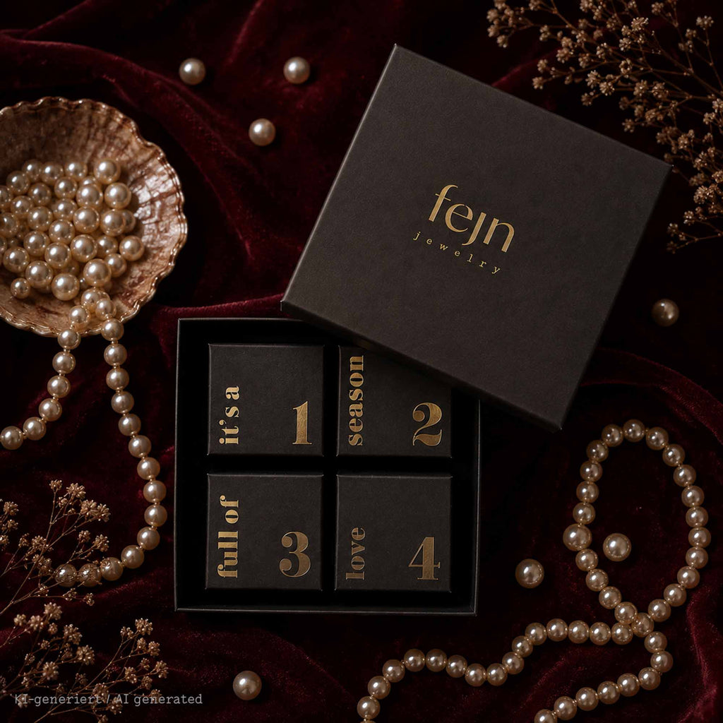 fejn jewelry Adventskalender  mit Perlenschmuck– Schwarze Schmuck-Geschenkbox mit 4 nummerierten Schachteln in goldener Schrift vor weihnachtlicher Hintergrundkulisse mit Perlen