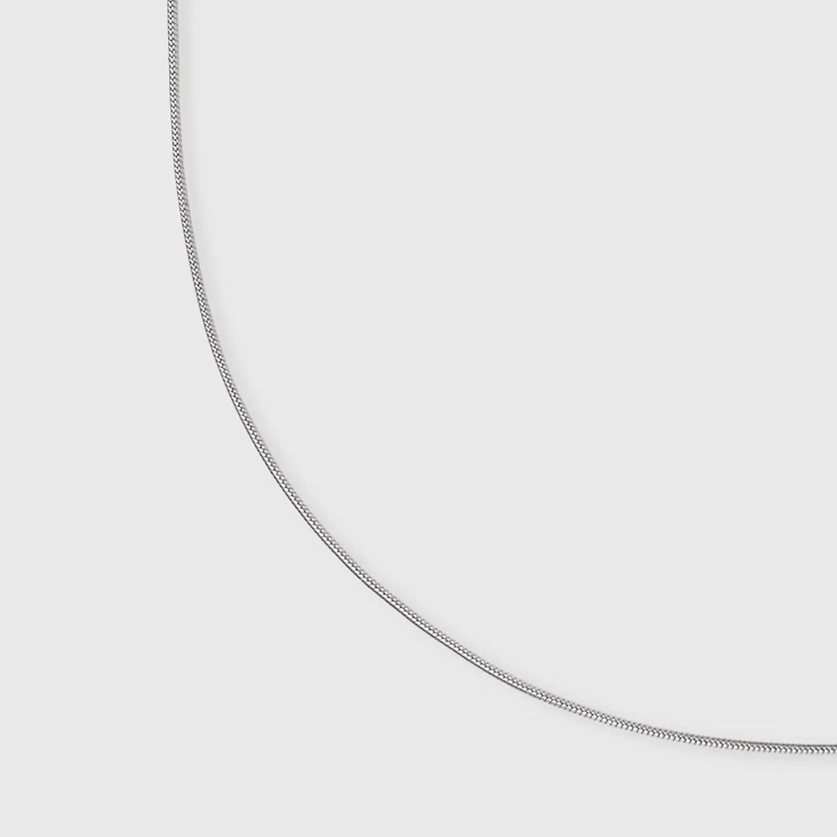 Detailaufnahme der flachen Struktur und der glänzenden Oberfläche der silbernen fejn Schlangenkette auf weißem Hintergrund.
