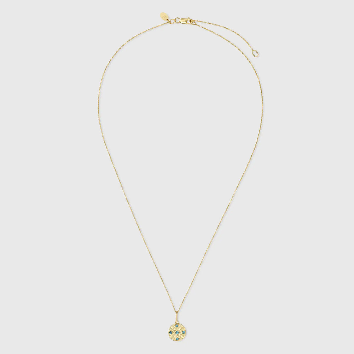 Runder Kettenanhänger aus 14k Echtgold im Art-Déco-Stil mit Sonnenstrahlen-Prägung und fünf blau funkelnden Topasen an einer feinen Goldkette vor hellem Hintergrund.