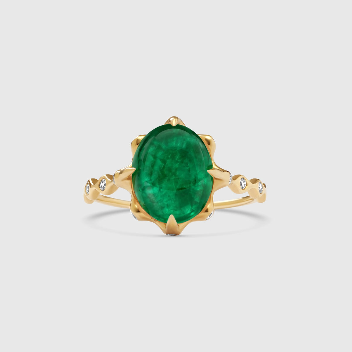Eleganter Goldring aus Echtgold mit einem ovalen, grün leuchtenden Smaragd im Cabochon-Schliff und seitlich besetzten Diamanten im Art-Déco-Stil vor hellem Hintergrund.