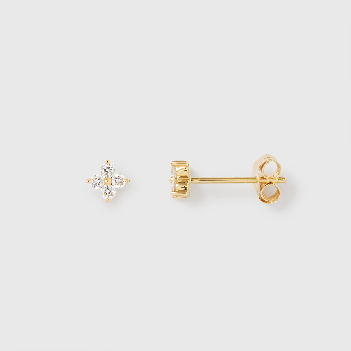 Nahaufnahme eines Paares goldener Ohrstecker im Diamond Flower Design auf hellem Hintergrund. Der linke Ohrstecker zeigt die Vorderansicht mit vier funkelnden Diamanten in einer Blütenform. Der rechte Ohrstecker zeigt die Seitenansicht mit Stift und Ohrmutter. Die Fassung ist aus poliertem Gelbgold.