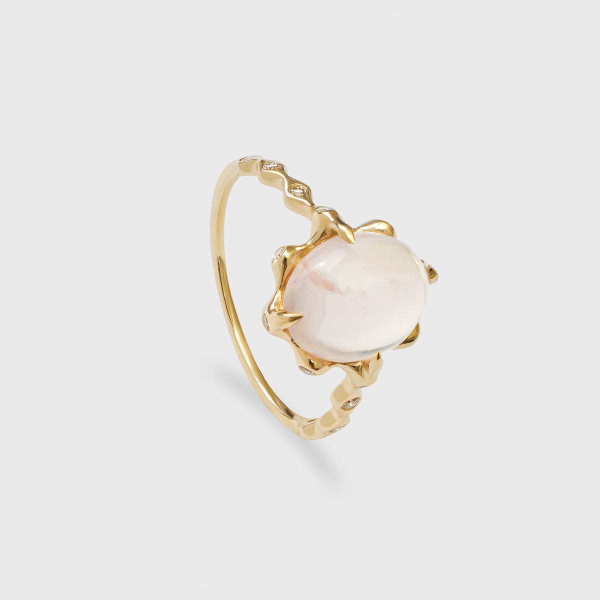 Nahaufnahme eines goldenen Rings im Art-Déco-Stil, der schräg von der Seite fotografiert wurde. Der Ring ist mit einem großen, ovalen Rosenquarz  besetzt, der von einer stilisierten, wellenförmigen Goldfassung gehalten wird. Die schmale Ringschiene hat ein welliges Design und ist mit kleinen, funkelnden Diamanten besetzt. Das Schmuckstück wird vor einem schlichten, hellgrauen Hintergrund präsentiert.